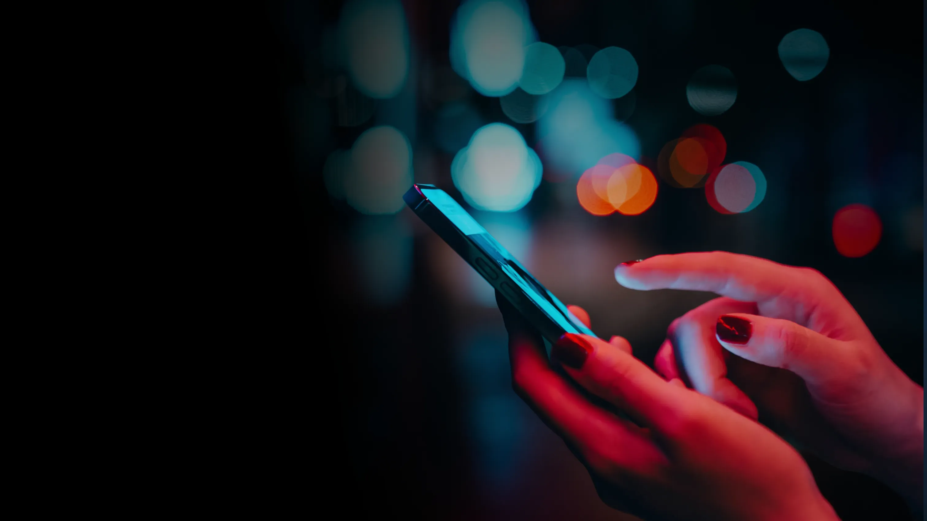 Hands holding a smartphone against blurred city lights at night
